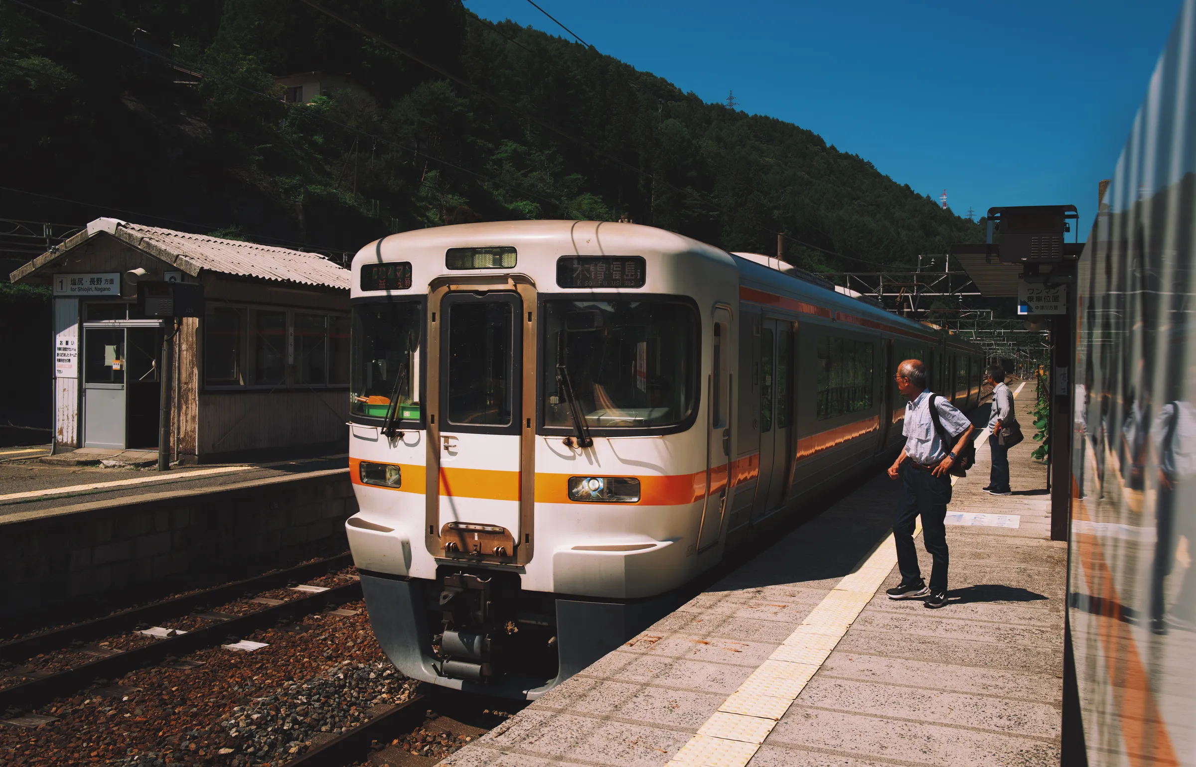 A local JR train at a small mountain station, a man waiting alone on the platform