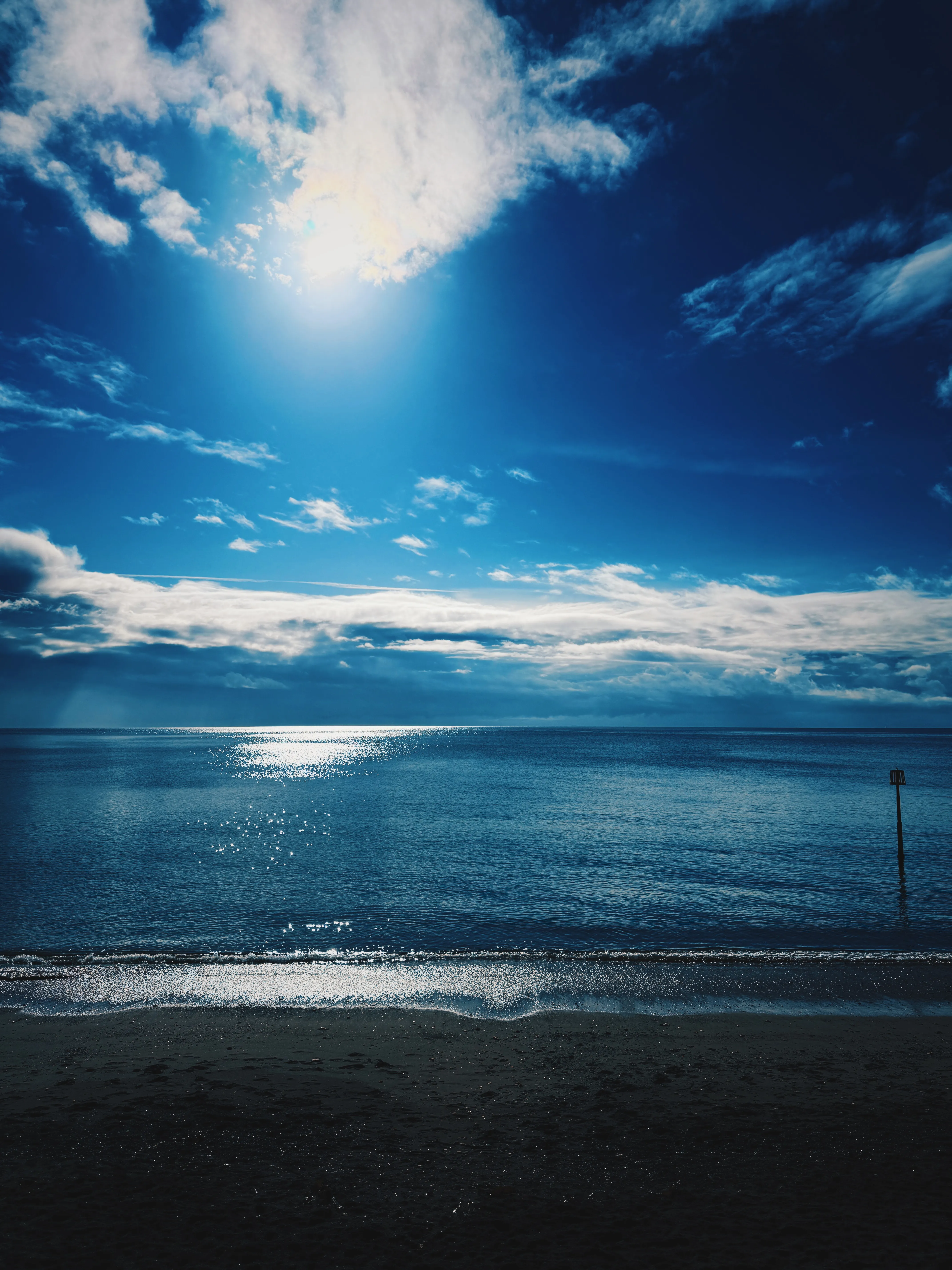Vivid lapis-blue sky over a calm dark teal sea, stone slipway with metal railings in the foreground left