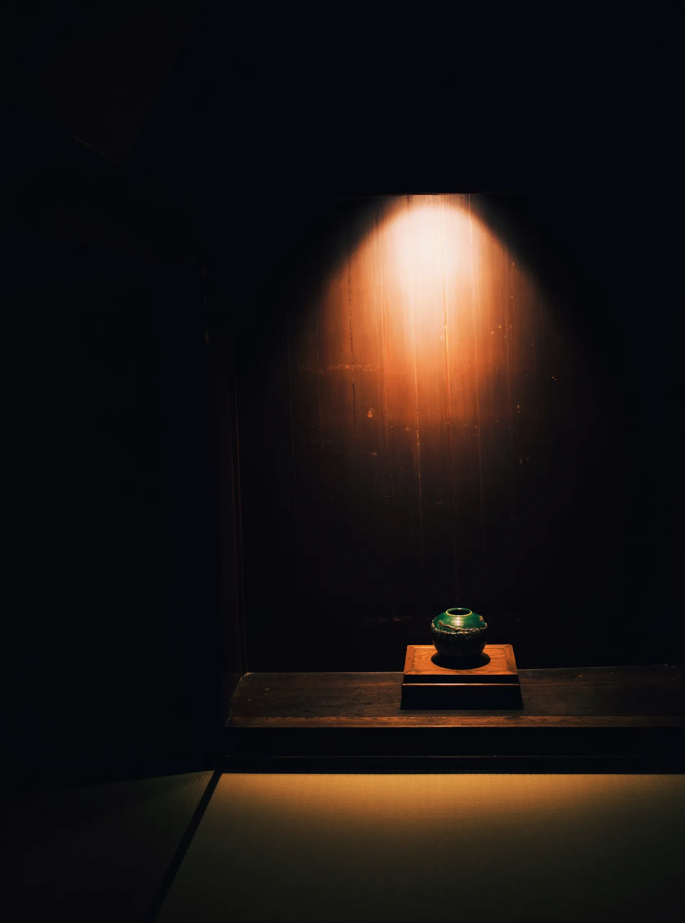 A ceramic bowl on a lacquered stand, lit by a single warm spotlight against dark timber walls