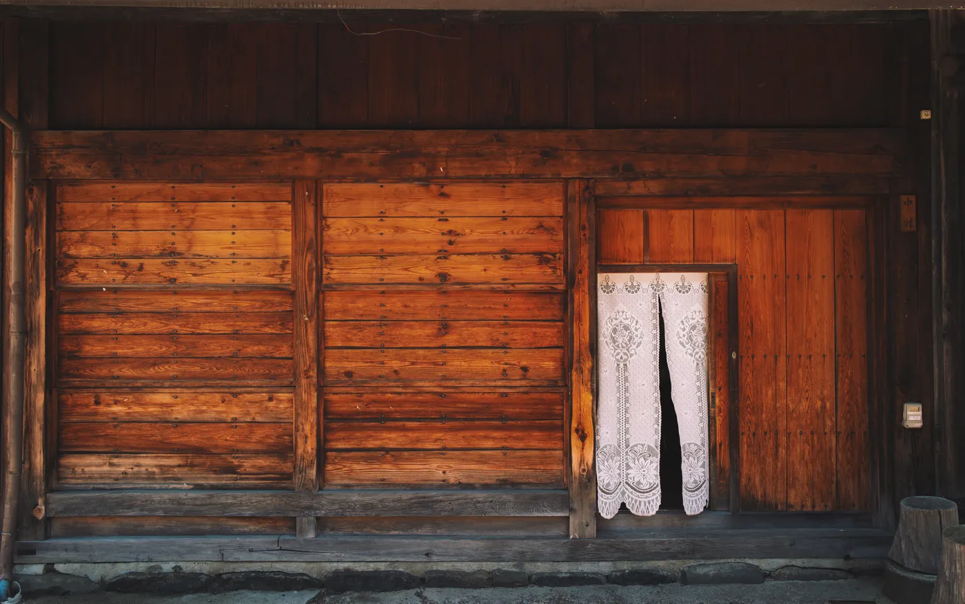 A white lace noren curtain hanging in a timber doorway of a post town building