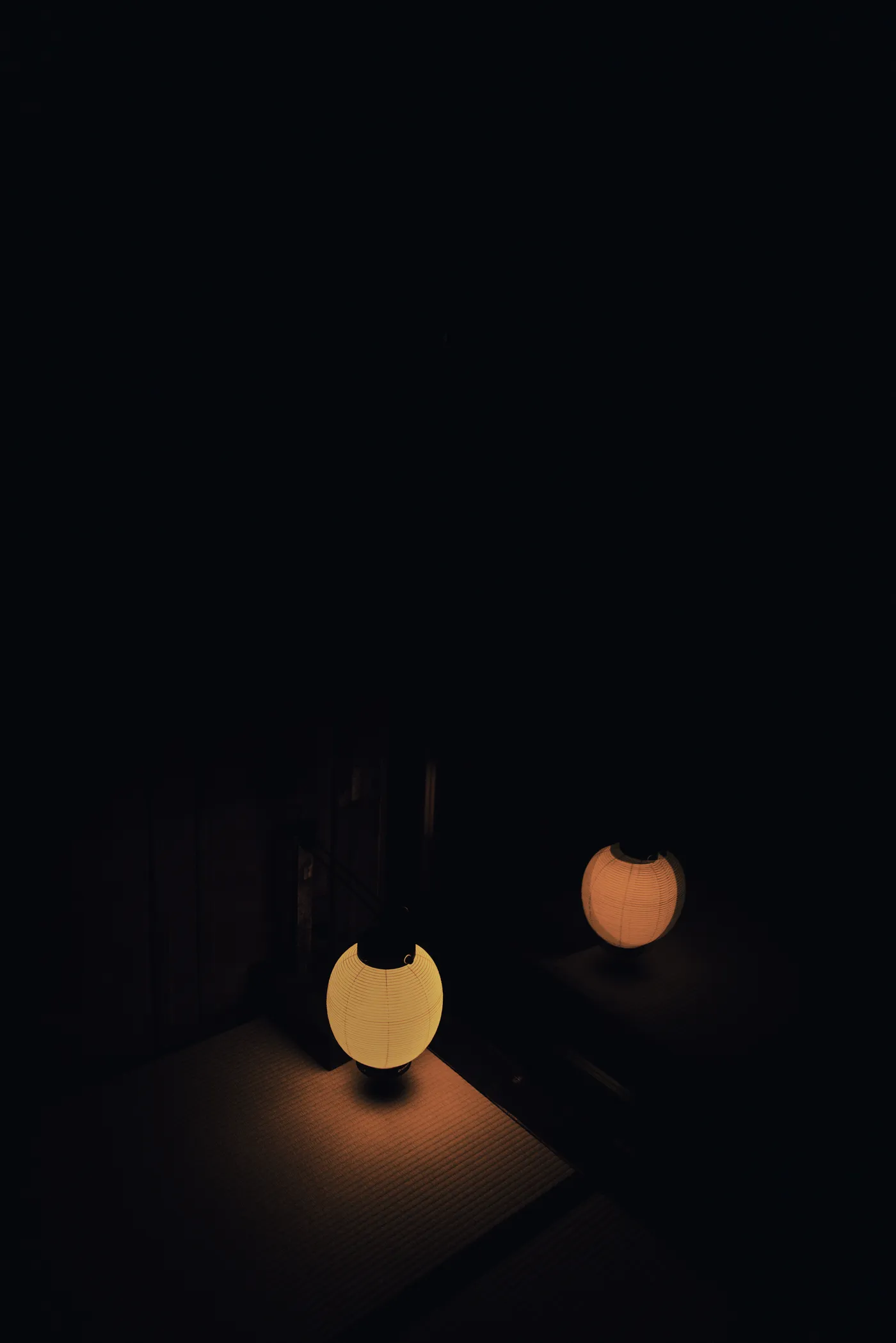 Two paper lanterns glowing against total darkness at a traditional inn, Magome
