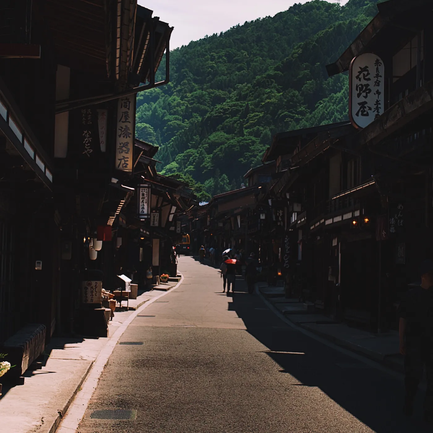 Narai main street receding into distance, dark timber buildings framing both sides, a figure with a red umbrella far ahead