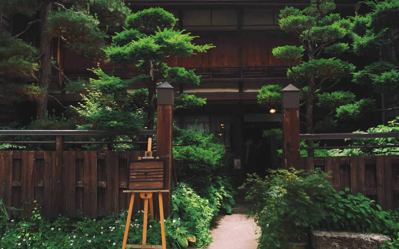 Entrance to a traditional ryokan with lush pine garden and an artist's easel in the foreground