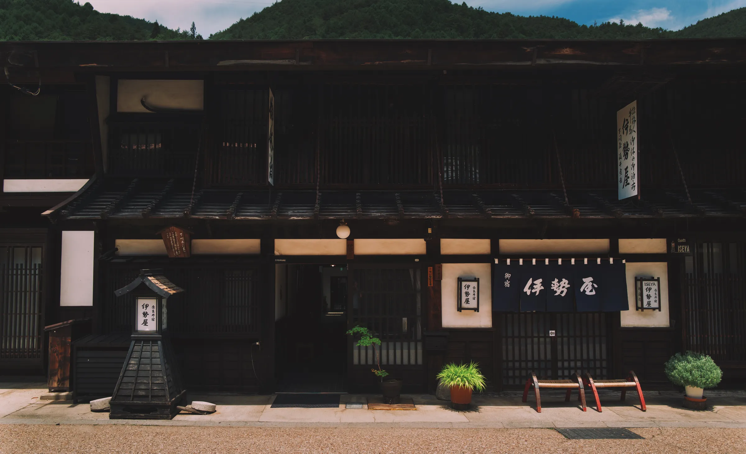 Traditional merchant house facade in Narai post town, dark timber and white plaster, Japanese signage, mountains behind