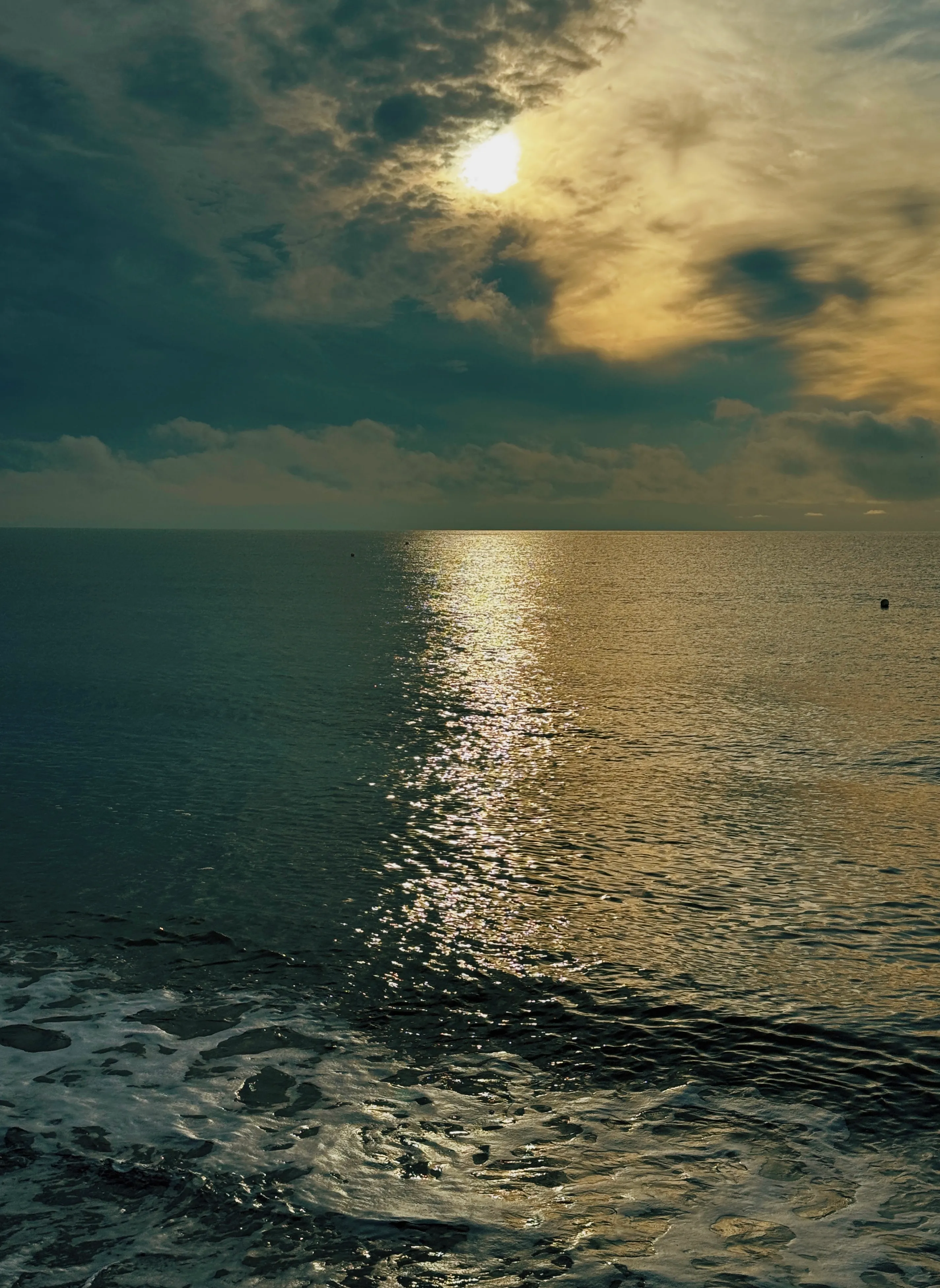 Golden sun path across a teal morning sea, two channel marker buoys in the middle distance