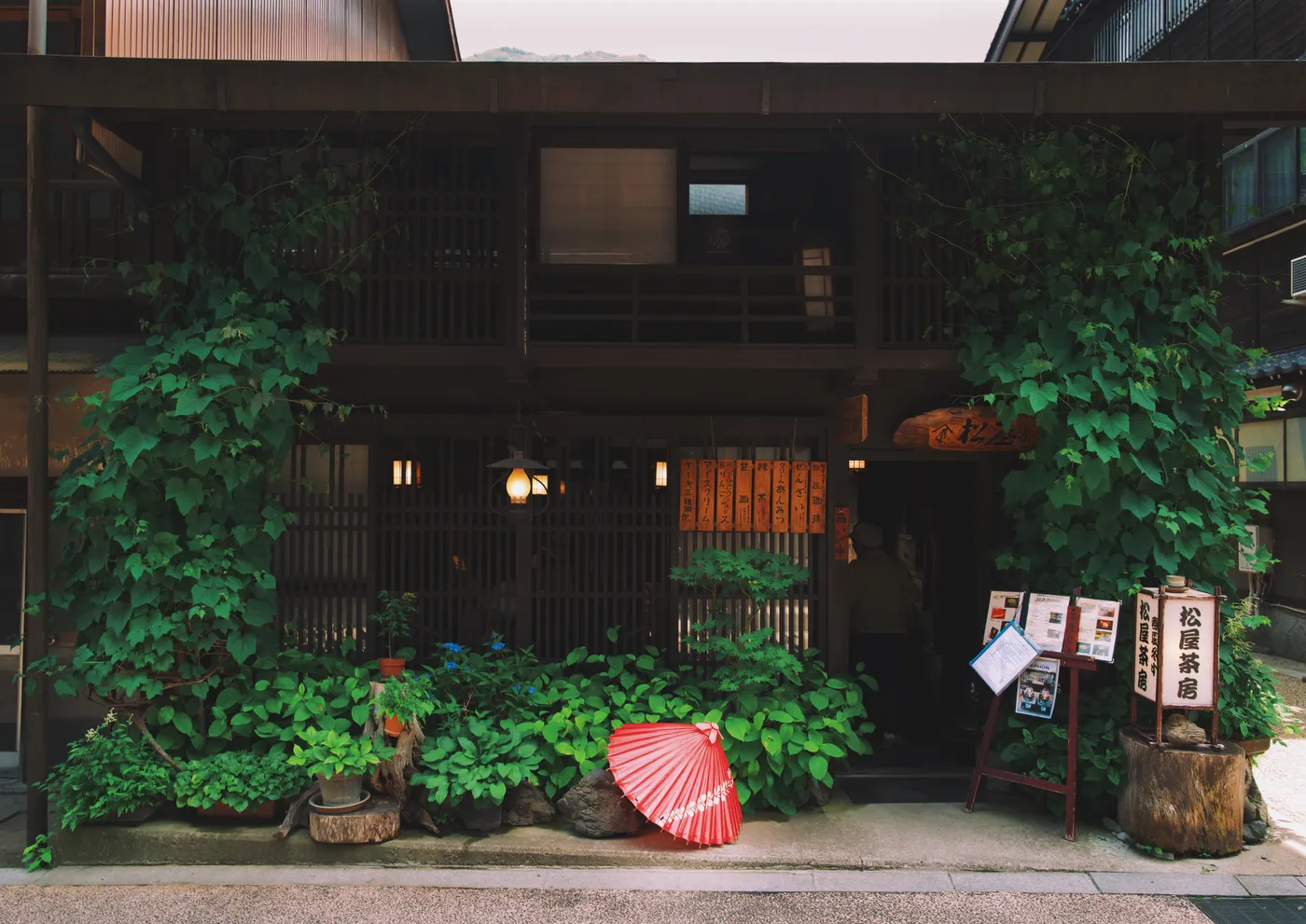 Restaurant facade draped in ivy with a red wagasa umbrella at the entrance and warm amber lantern light