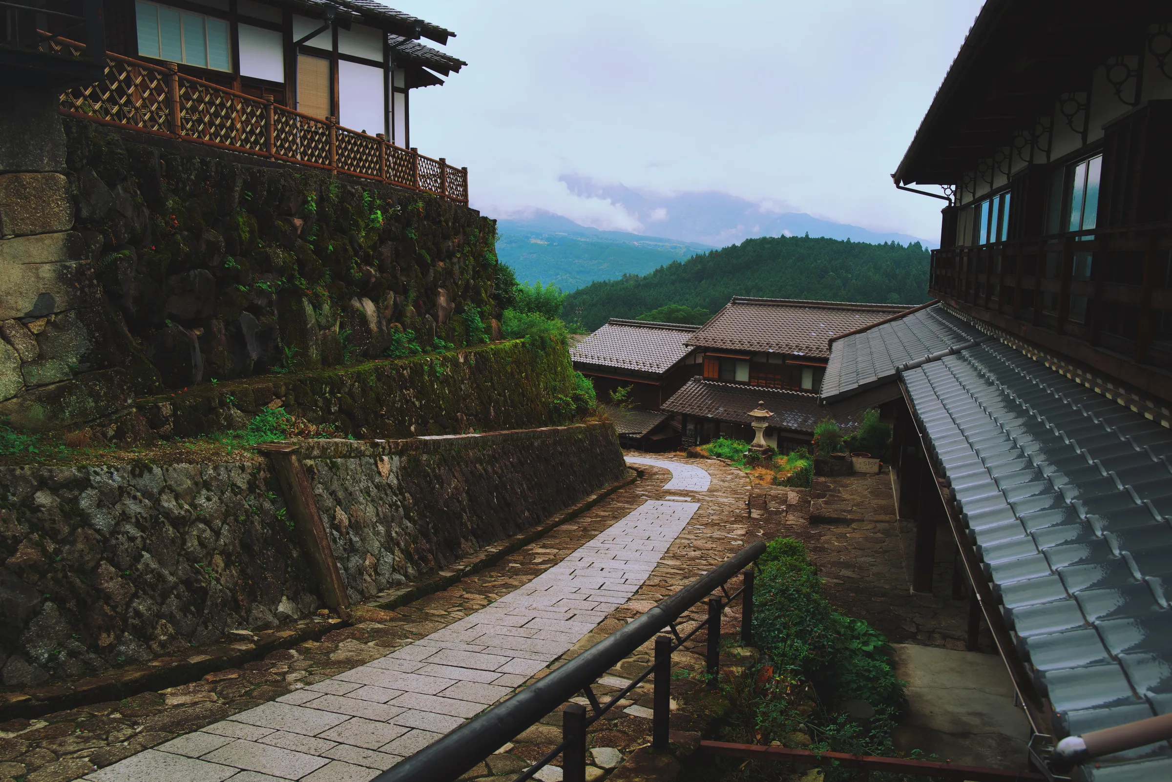 Magome post town viewed from above, stone retaining walls and grey-tiled rooftops, mountains dissolving in cloud