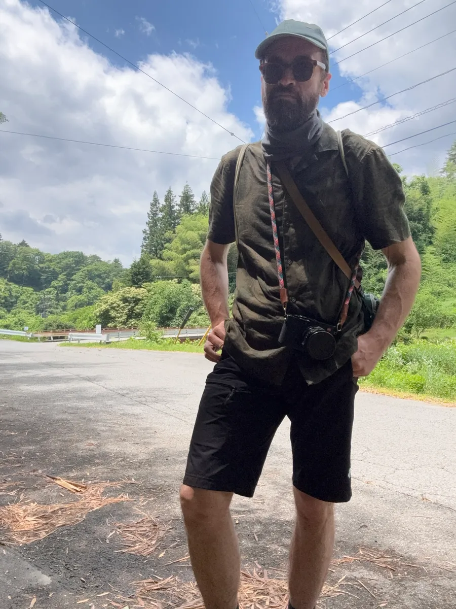 Self-portrait on a country road, Leica Q2 camera around neck, blue sky and green mountains