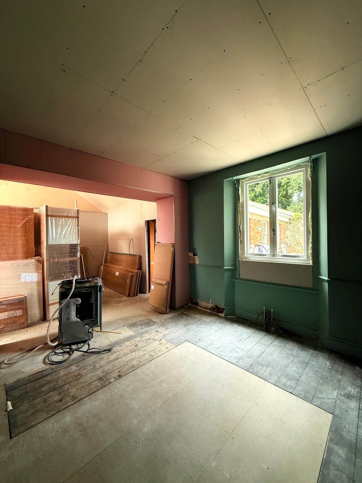 View of what used to be the dining room through into the kitchen with a new window installed in the previous opening and a shim underneath it where the cabinetry will come to.