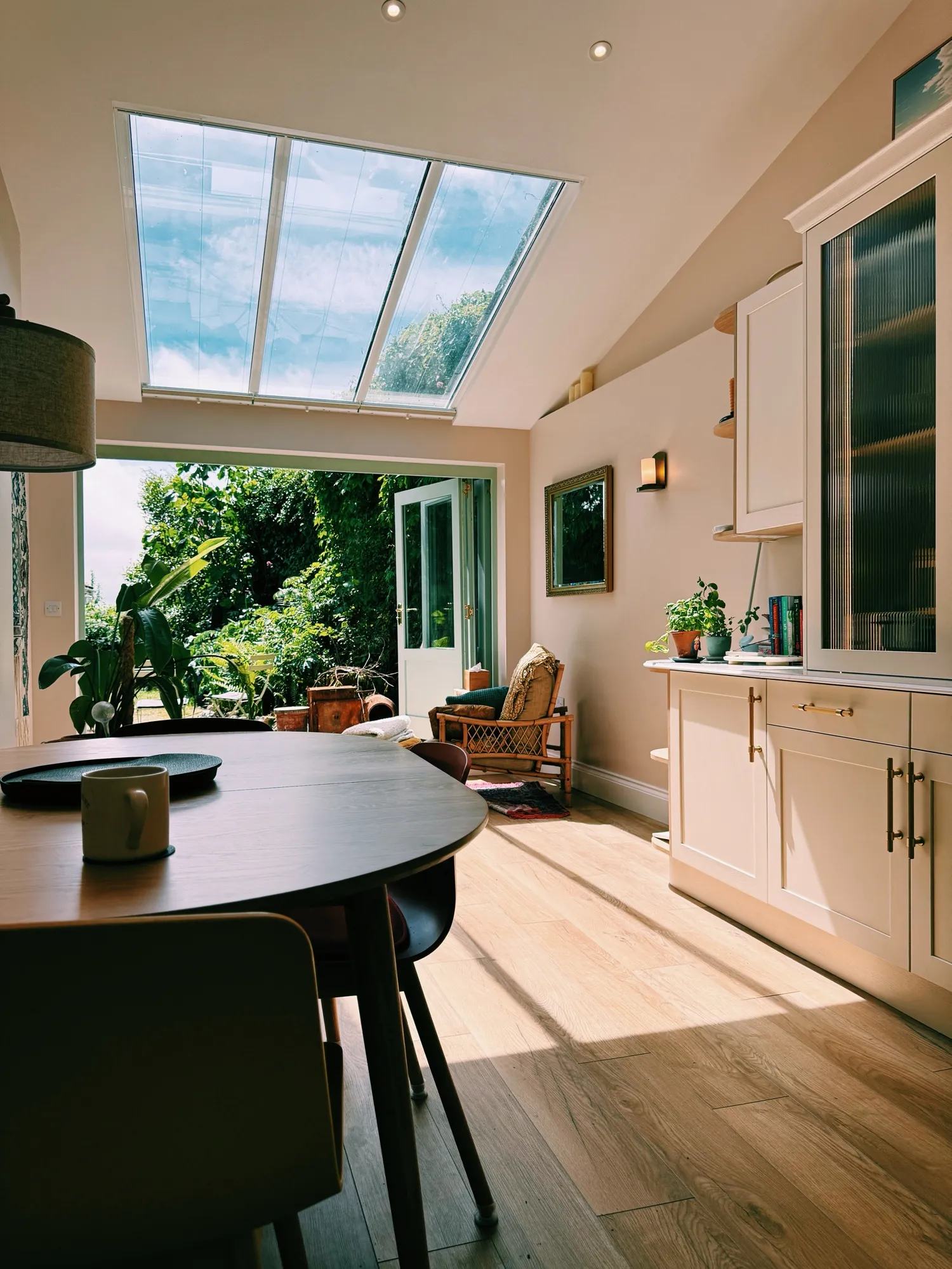 The finished kitchen — reeded glass cabinet doors, a mirror reflecting the garden's greenery, sunlight coming in.